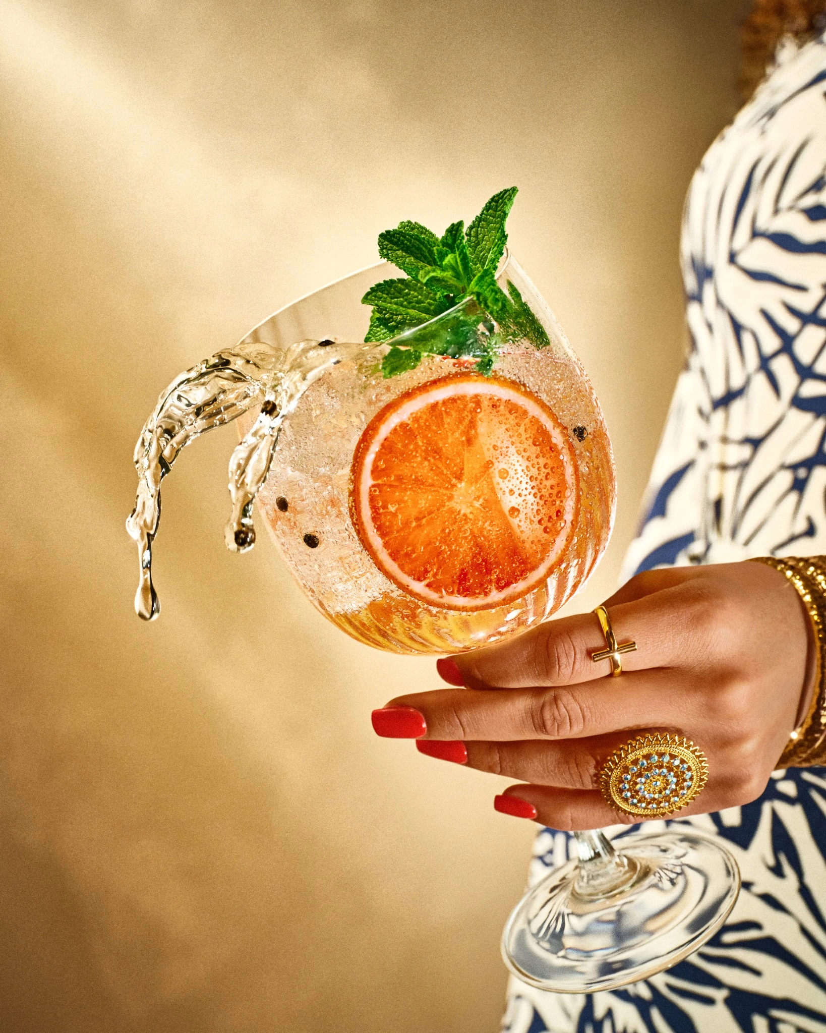 Cocktail with orange and mint held in a jewelled hand